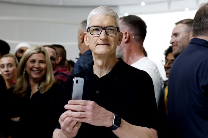AppleのティムクックCEOがiPhoneを手に持ち、イベント会場で関係者に囲まれている様子